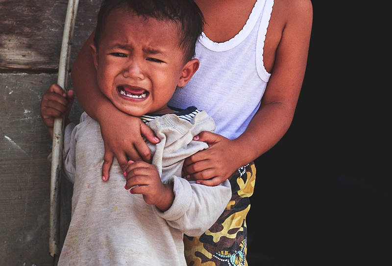 a crying toddler is held by a sybling